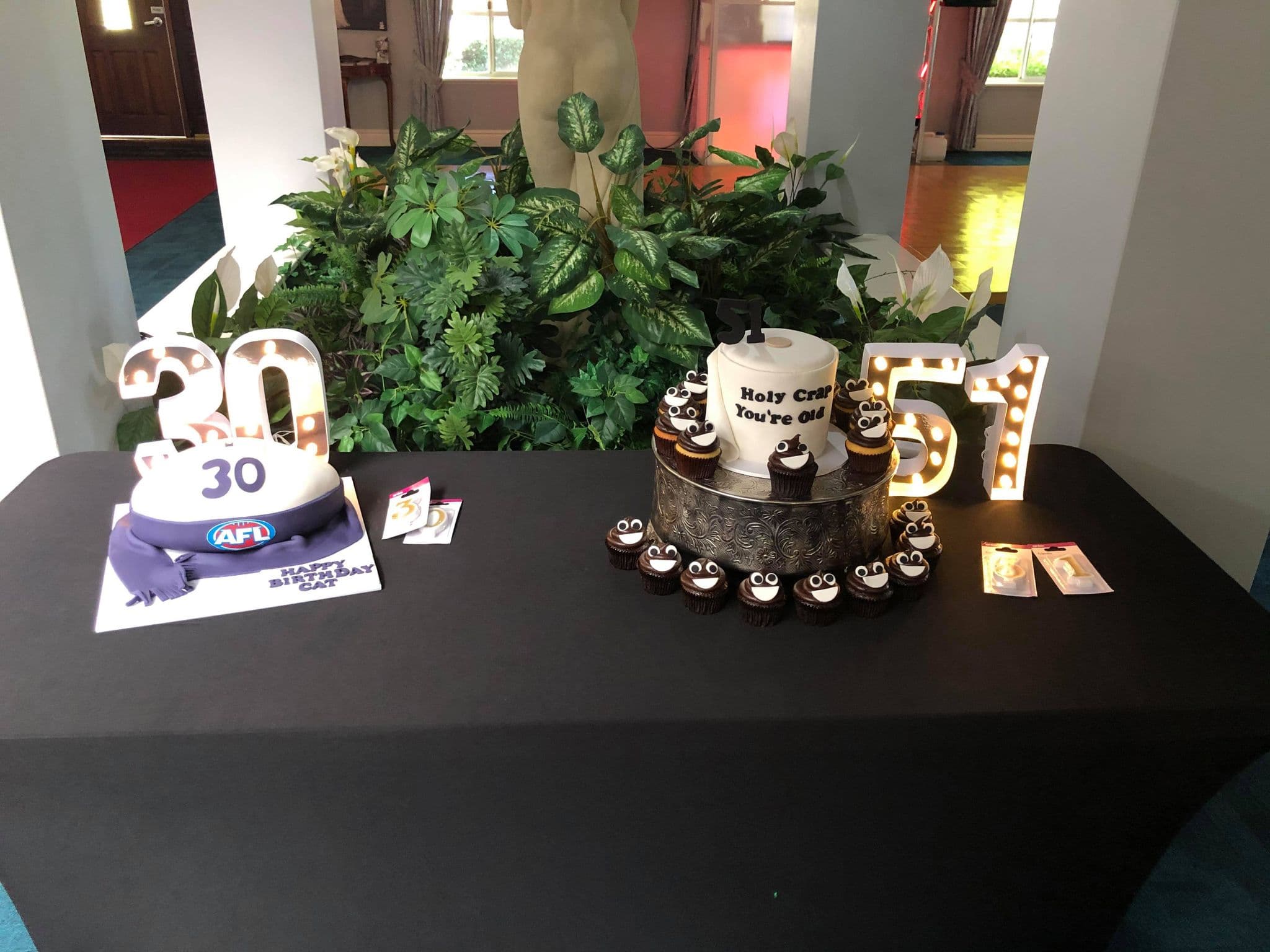 Milestone birthday cake table with light-up numbers and cupcakes, set up in the manor's entrance hall