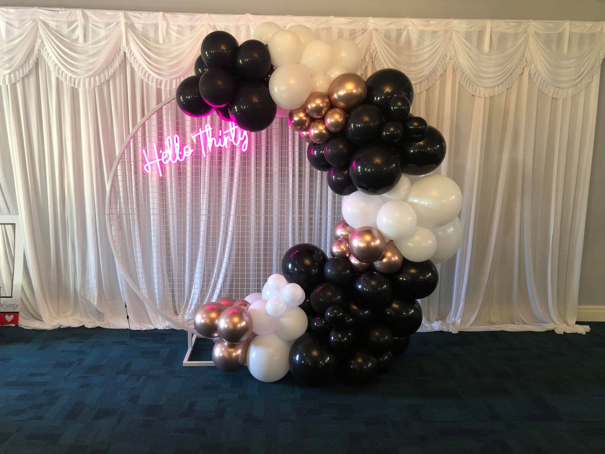 Black, white and rose gold balloon garland arch with a 'Hello Thirty' neon sign backdrop