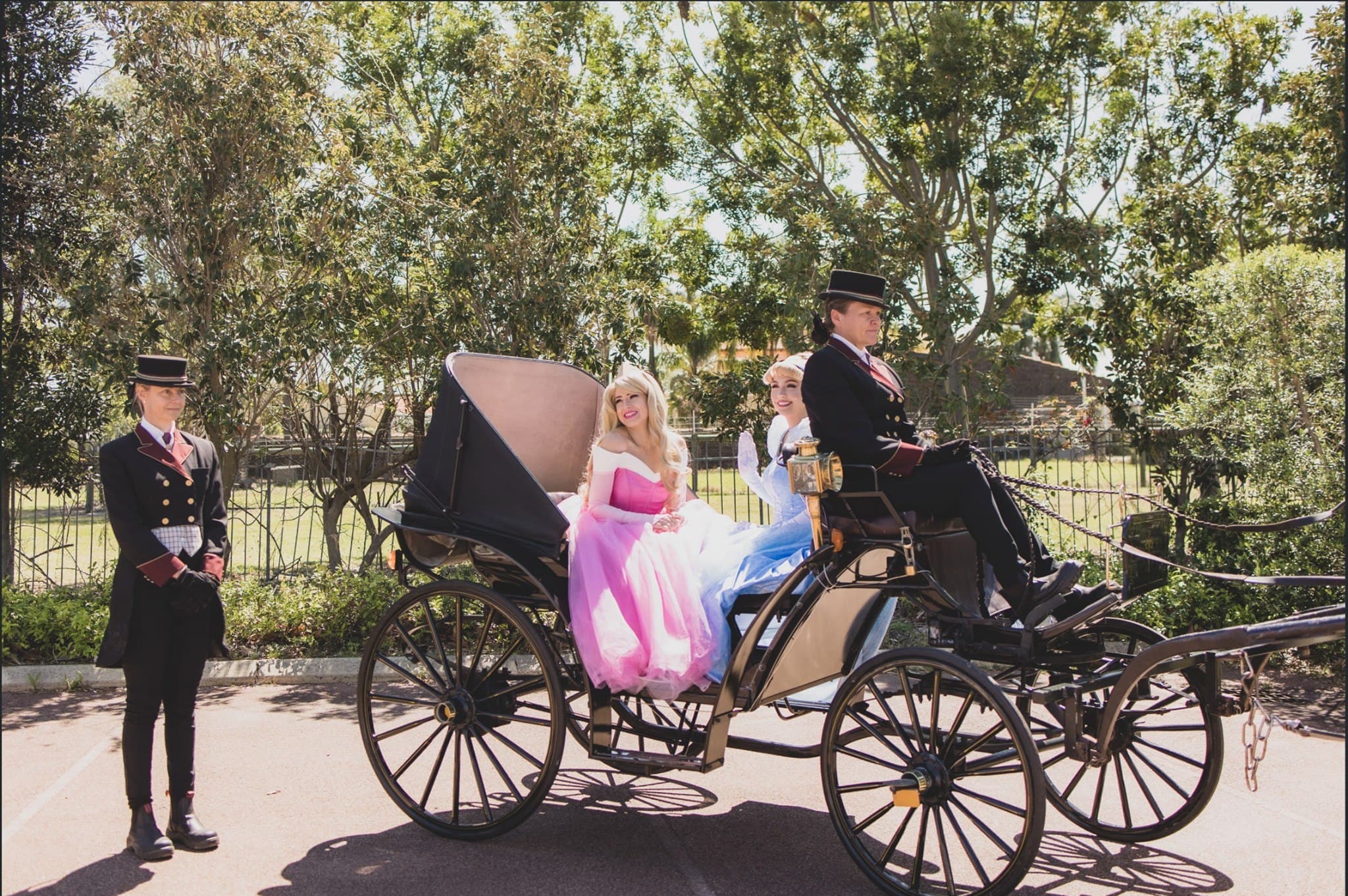 Performers in Disney-princess-style costume gowns riding in a horse-drawn carriage with a costumed driver and footman