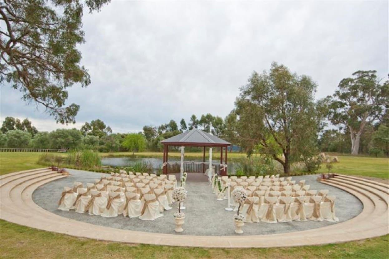 Wide view of the stepped amphitheater seating and gazebo beside the pond, dressed with cream and gold chair sashes