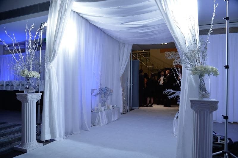 White-draped winter entrance with fairy lights and frosted branch arrangements on plinths